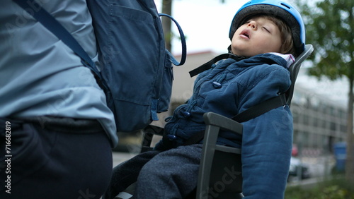 Child Asleep in Bicycle Backseat, Wearing Helmet during Ride. Little boy napping outside