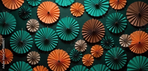  a group of orange and green paper fans hanging on a wall next to a wall of other orange and green paper fans on a green wall behind a green wall.