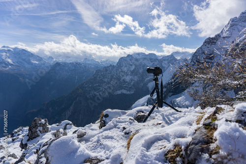 A camera on a tripod poised to capture the beauty of a snow-capped mountain range under a bright sky. © Marcel