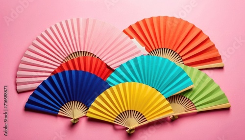  a group of colorful paper fans sitting on top of a pink surface with the colors of the rainbow in the middle of the fan  on top of a pink background.