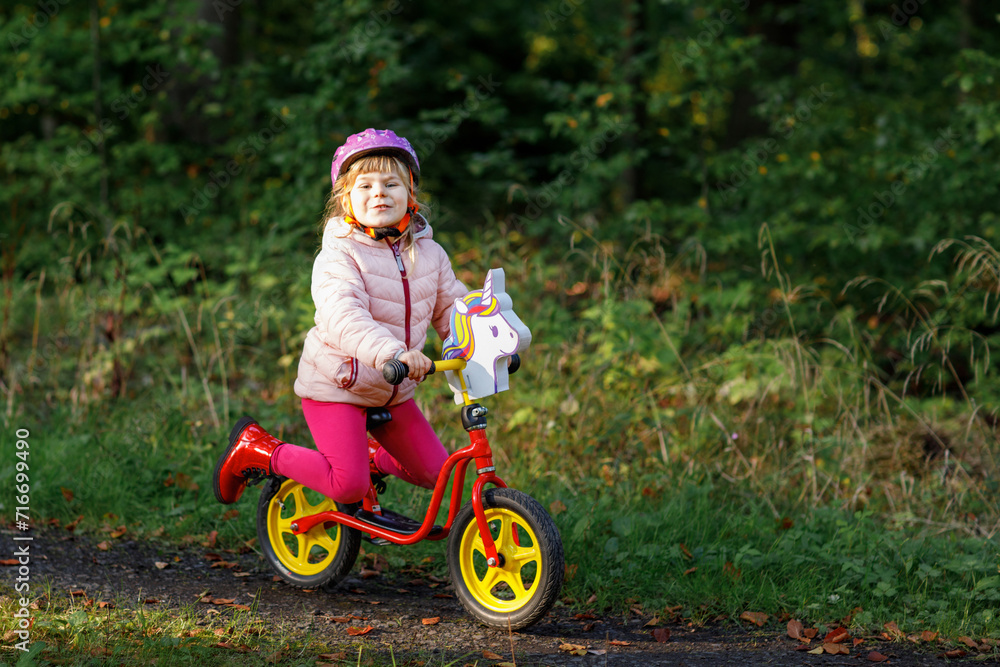 Child riding balance bike. Kids on bicycle in sunny forest. Little girl enjoying to ride glider bike on warm day. Preschooler learning to balance on run bicycle in safe helmet. Sport activity Child riding balance bike. Kids on bicycle in sunny forest. Little girl enjoying to ride glider bike on warm day. Preschooler learning to balance on run bicycle in safe helmet. Sport activity