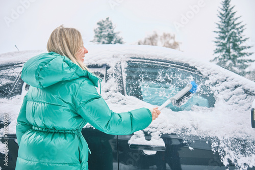 Woman remove her car from snow, Clean car window in winter from snow emoving snow from car windshield. Scraping ice. Winter season car window cleaning. photo