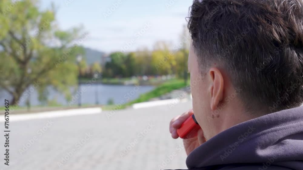 A person using a vape or e-cigarette in the background of an alley in a park A person using a vape or e-cigarette in the background of an alley in a park