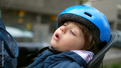 Little boy asleep in bicycle's backseat wearing helmet. Child napping after falling asleep while in bike's ride, deep afternoon slumber