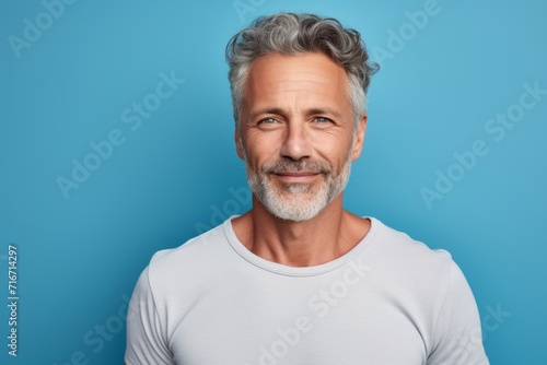 Portrait of a tender man in his 50s dressed in a casual t-shirt against a pastel blue background. AI Generation