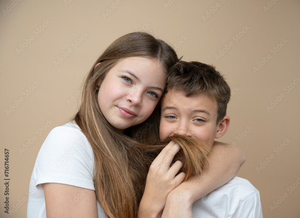 beautiful pretty 14 years old girl with her cute and cool 11 years old brother in front of brown background, brother and sister love beautiful pretty 14 years old girl with her cute and cool 11 years old brother in front of brown background, brother and sister love