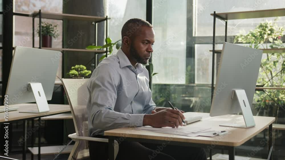 African american mature senior businessman 40s ethnic man sit at office desk middle-aged banker manager write notes business documents writing text on papers counting loan bills enter data at computer African american mature senior businessman 40s ethnic man sit at office desk middle-aged banker manager write notes business documents writing text on papers counting loan bills enter data at computer