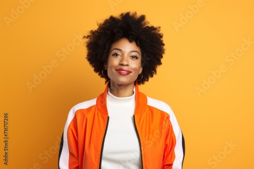 Portrait of a content afro-american woman in her 40s sporting a stylish varsity jacket against a pastel orange background. AI Generation