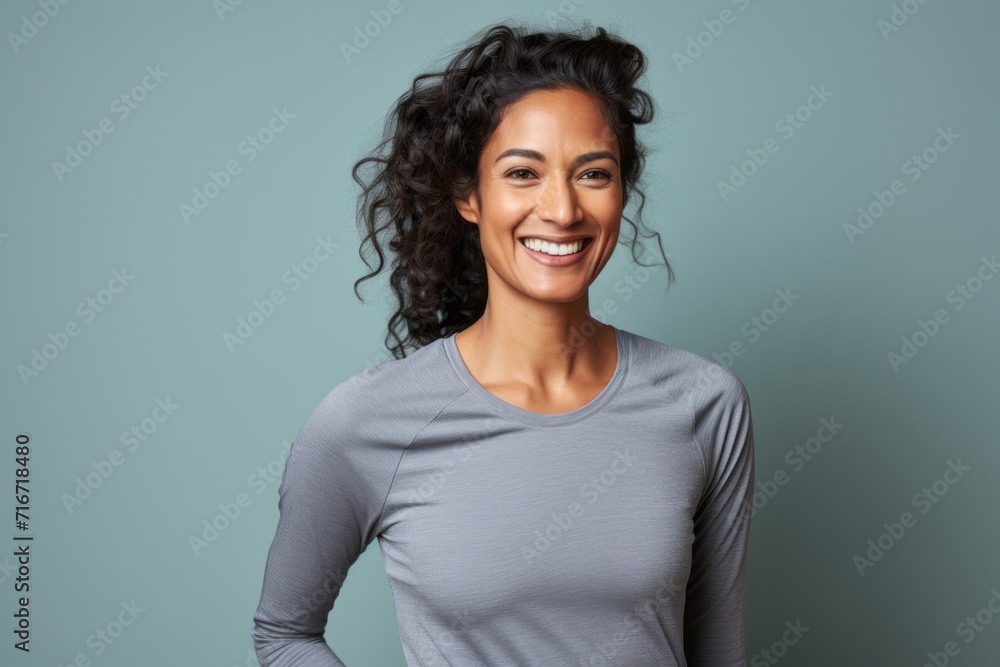 Obraz premium Portrait of a smiling indian woman in her 30s wearing a moisture-wicking running shirt against a pastel gray background. AI Generation