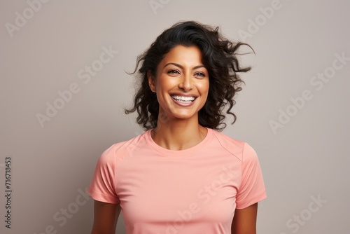 Portrait of a smiling indian woman in her 30s wearing a moisture-wicking running shirt against a pastel gray background. AI Generation photo