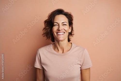 Portrait of a smiling woman in her 40s sporting a vintage band t-shirt against a pastel brown background. AI Generation © CogniLens