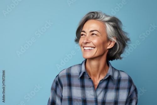 Portrait of a cheerful woman in her 50s wearing a comfy flannel shirt against a soft blue background. AI Generation