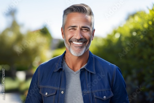 Portrait of a smiling man in his 50s sporting a rugged denim jacket against a soft blue background. AI Generation