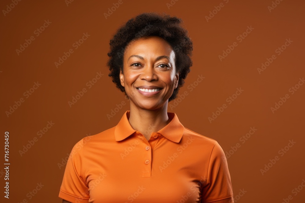 Obraz premium Portrait of a merry afro-american woman in her 40s wearing a sporty polo shirt against a soft brown background. AI Generation