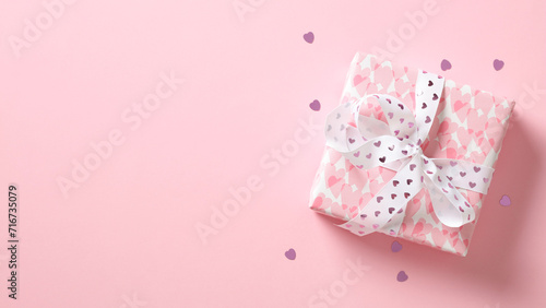 Pink gift box with ribbon bow and hearts on pastel pink background. Flat lay, top view. Happy Valentine's Day concept.