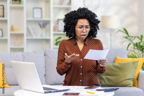 Φωτογραφία Shocked african american woman sitting on sofa at home, working with laptop and