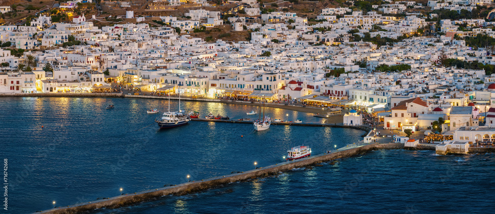 Panoramic aerial view of the town of Mykonos island with the busy promenade at the old harbour during dusk, Cyclades, Greece