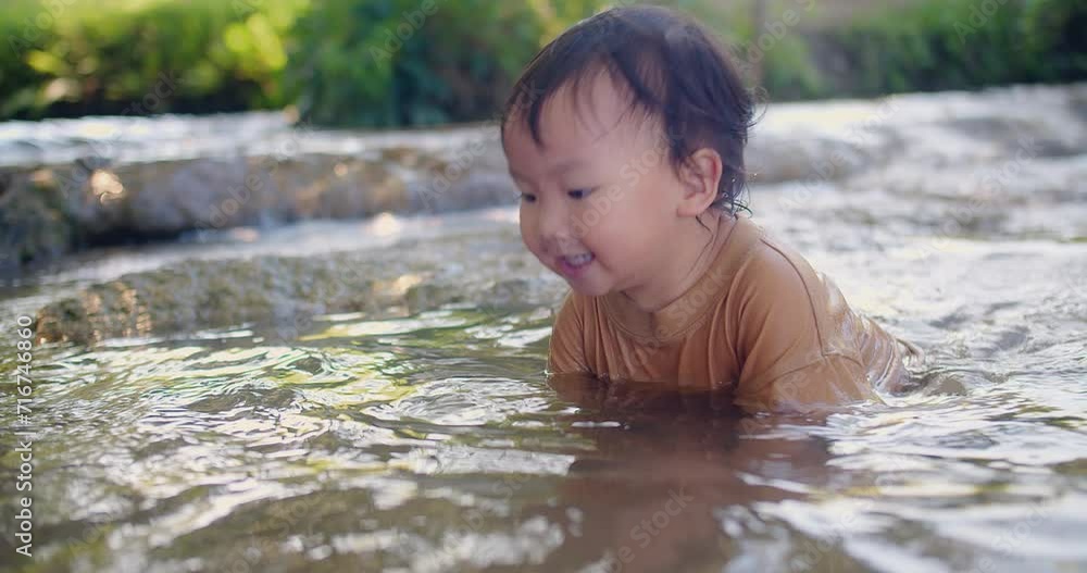 A curious toddler in a brown shirt joyfully explores the sensations of splashing water experiences the joy of water play in a shallow stream, surrounded by lush vegetation A curious toddler in a brown shirt joyfully explores the sensations of splashing water experiences the joy of water play in a shallow stream, surrounded by lush vegetation