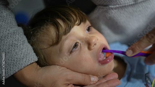 Parent brushes child's teeth during night routine before bedtime. Close-up kid face and mouth brushing dental hygiene ritual