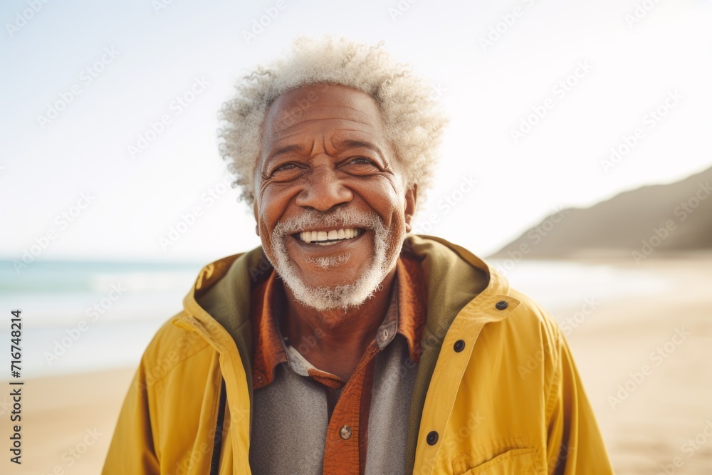 Portrait of a satisfied afro-american elderly man in his 90s wearing a warm parka against a sandy beach background. AI Generation