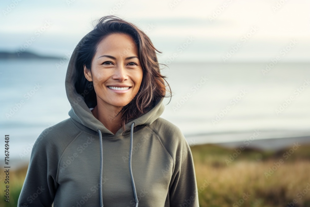 Portrait of a smiling woman in her 30s sporting a comfortable hoodie against a serene seaside background. AI Generation