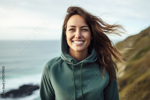 Portrait of a smiling woman in her 30s sporting a comfortable hoodie against a serene seaside background. AI Generation