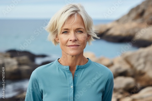 Portrait of a content woman in her 60s wearing a sporty polo shirt against a rocky shoreline background. AI Generation