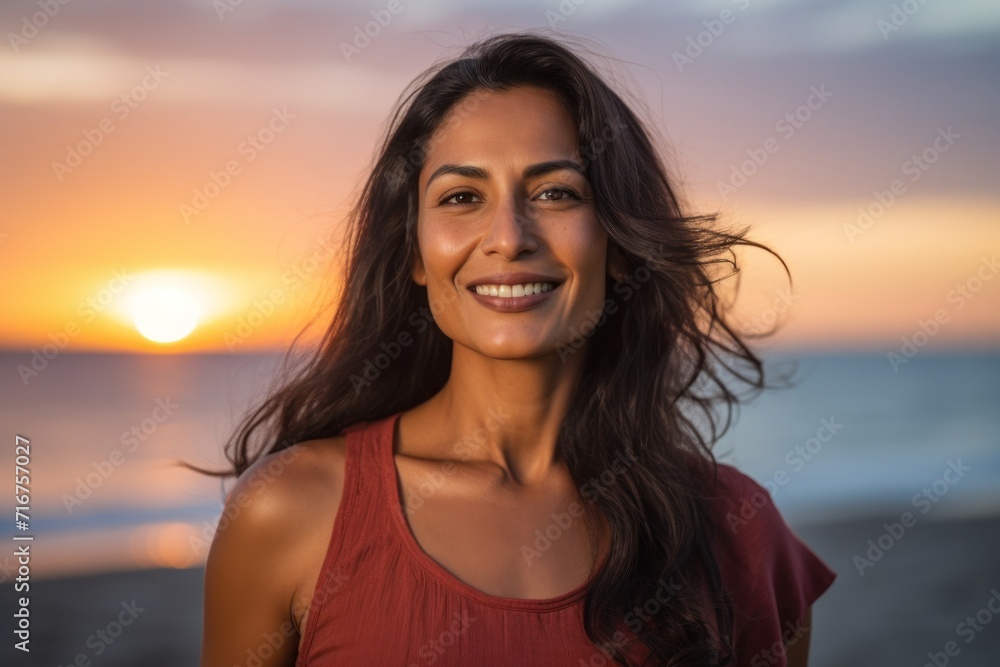Portrait of a glad indian woman in her 30s dressed in a casual t-shirt against a vibrant beach sunset background. AI Generation