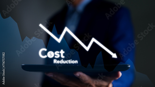 Businessman working on company cost saving. Cost wording on decreasing coins stacking with the down arrow. Cost Management, Economy recession, low budget, Effective business, Cost reduction concept. photo