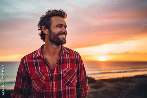 Portrait of a happy man in his 30s dressed in a relaxed flannel shirt against a vibrant beach sunset background. AI Generation