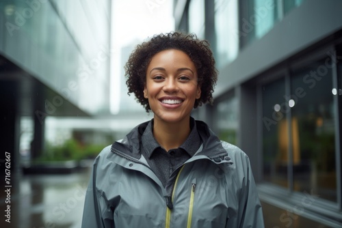 Portrait of a satisfied afro-american woman in her 30s sporting a waterproof rain jacket against a sophisticated corporate office background. AI Generation photo