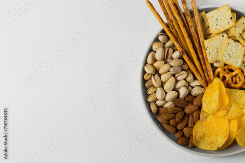 Salty snacks on a white background. Almonds, pistachios, Crackers, potato chips and mini pretzels in the grey plat. Party mix.Assortment of crispy appetizers. copy space. top view