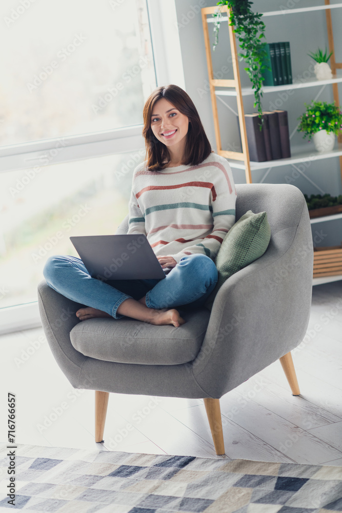 Full size vertical photo of positive nice girl sit chair barefoot use wireless netbook morning apartment indoors Full size vertical photo of positive nice girl sit chair barefoot use wireless netbook morning apartment indoors