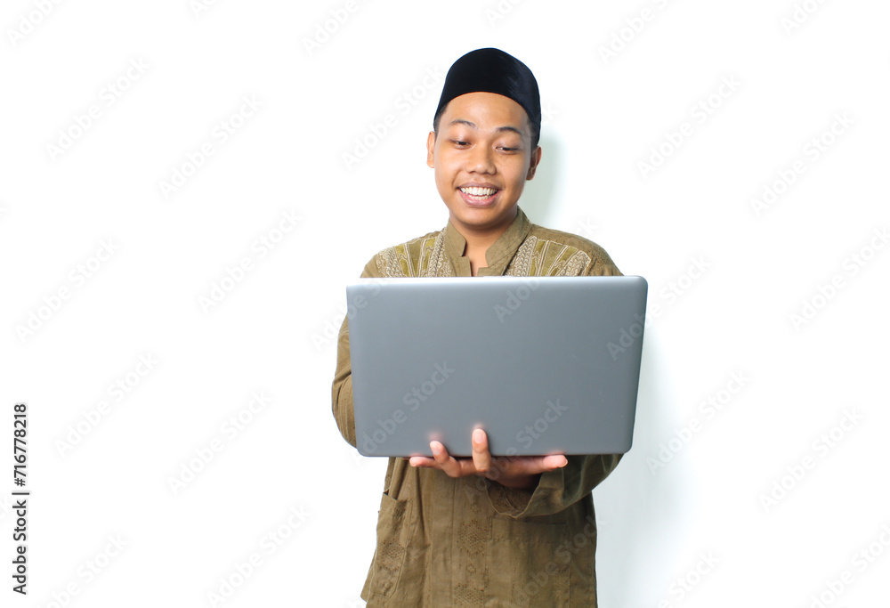 cheerful asian muslim man wearing islamic dress holding laptop isolated on white background cheerful asian muslim man wearing islamic dress holding laptop isolated on white background