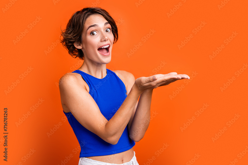 Photo of adorable excited girl dressed blue top open mouth holding arms empty space isolated orange color background Photo of adorable excited girl dressed blue top open mouth holding arms empty space isolated orange color background