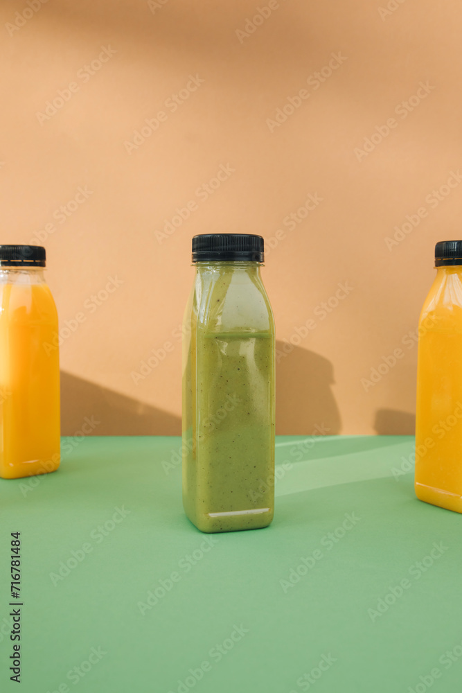 Fruit and vegetable smoothies in transparent plastic bottles. Green, orange smoothies on a brown-green background. The concept of healthy eating. Front view Fruit and vegetable smoothies in transparent plastic bottles. Green, orange smoothies on a brown-green background. The concept of healthy eating. Front view
