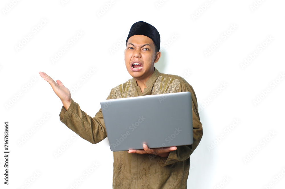 emotional asian muslim man presenting to beside with holding laptop wearing islamic clothes isolated on white background emotional asian muslim man presenting to beside with holding laptop wearing islamic clothes isolated on white background