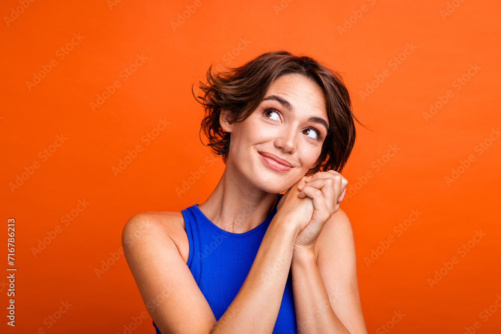 Photo of excited thoughtful lady wear blue singlet arms cheek looking empty space isolated orange color background Photo of excited thoughtful lady wear blue singlet arms cheek looking empty space isolated orange color background