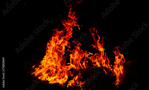 Bright flames rising and moving at dark nigh in blurred background.Orange fire flames.Burning red hot sparks rise  Fiery orange glowing flying particles.