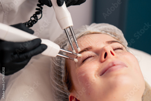 a close-up beautician conducts a microcurrent cosmetic procedure on a client's face in beauty salon