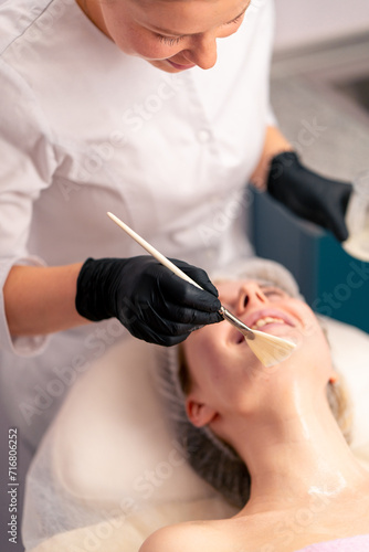 beautician in gloves applies a mask on the face of a client with a brush care for the skin