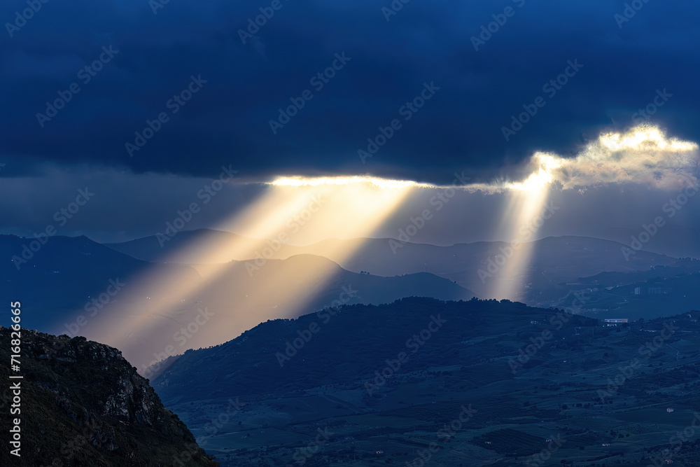 Caccamo, Sicily, Italy Beams of sunlight shine through the clouds illuminating the mountains at sunset.