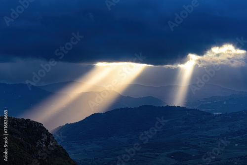 Caccamo, Sicily, Italy Beams of sunlight shine through the clouds illuminating the mountains at sunset.