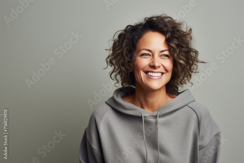Portrait of a cheerful woman in her 40s dressed in a comfy fleece pullover against a minimalist or empty room background. AI Generation © CogniLens