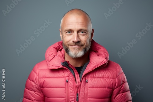 Portrait of a cheerful man in his 40s sporting a quilted insulated jacket against a minimalist or empty room background. AI Generation