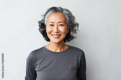 Portrait of a blissful asian woman in her 60s showing off a lightweight base layer against a minimalist or empty room background. AI Generation