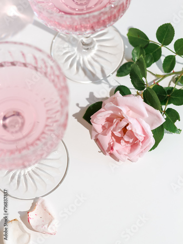 A pink rose and two glasses with rose drink on a white table, shot from above