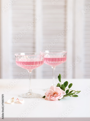 Two glasses with pink rose drinks and a pink rose on a white table