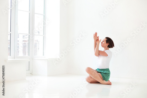 Young brunette female in white sportswear doing yoga while practicing mindfulness