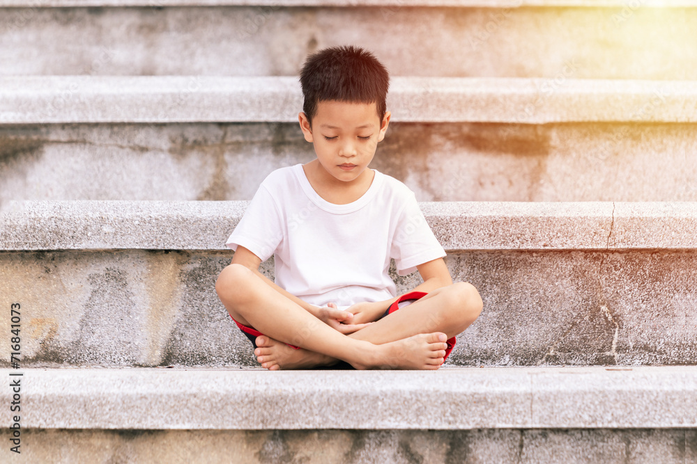 Asian kid meditating in the park. Cute little boy in meditation pose. Gymnastic, yoga and meditation for children.
